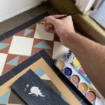 Filling and matching the color on chipped original Victorian tiles. Enamel tile restoration paint is being used on this white tile repair