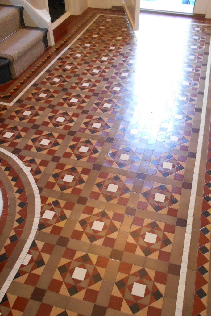attractive shiny Victorian geometric tiles in a hallway. Tiles are yellow, coffee, red, black and white. They where deep cleaned and waxed .